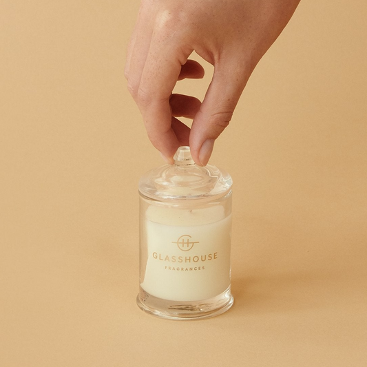 Hand holding a glasshouse candle against a beige background