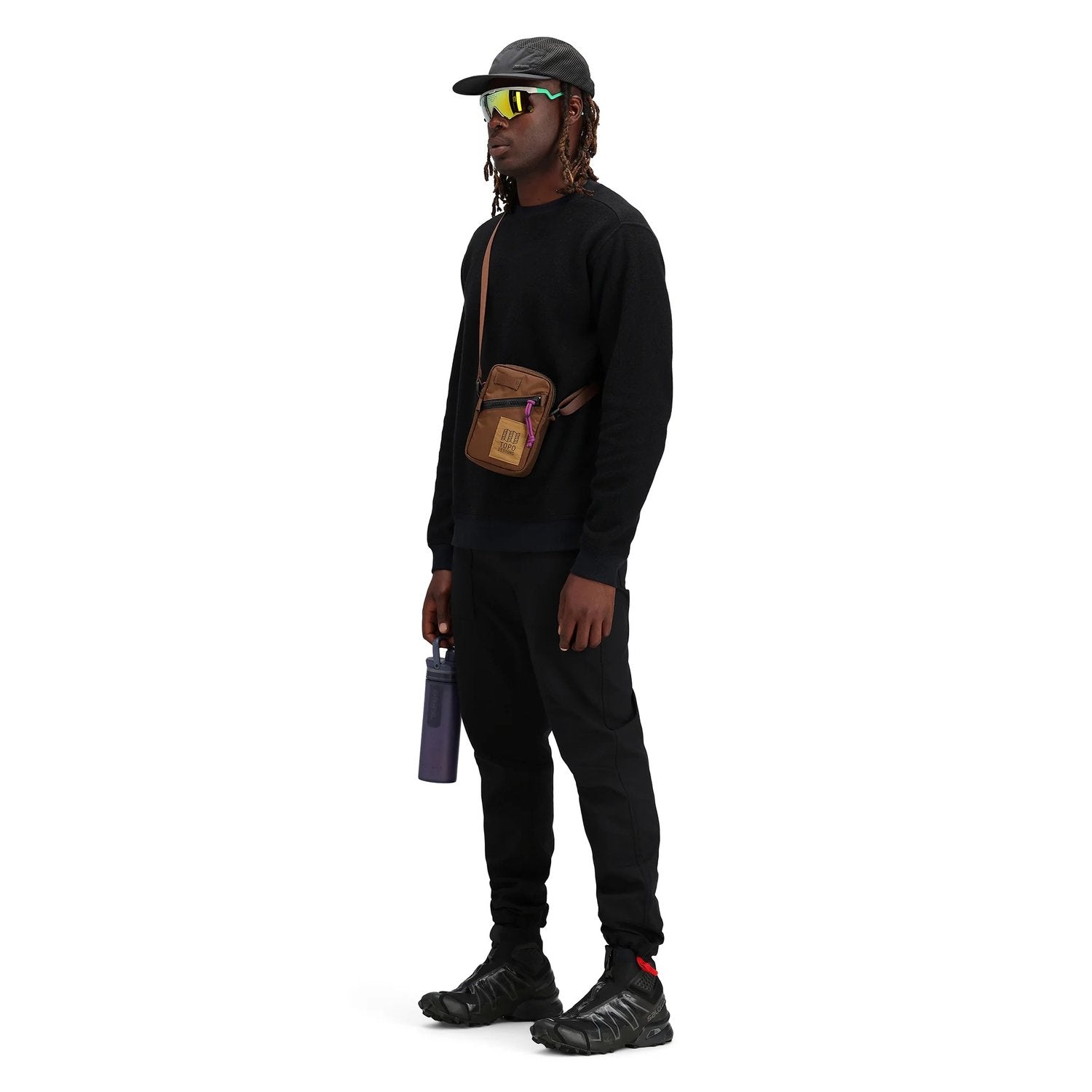 Person wearing a black outfit with a brown bag, standing against a white background