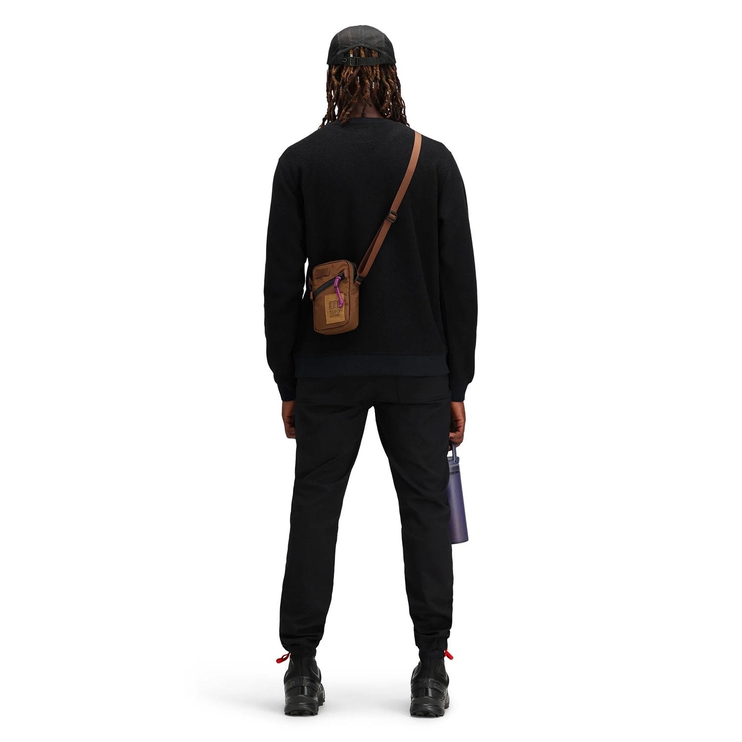 Person wearing a black outfit with a brown crossbody bag on a white background