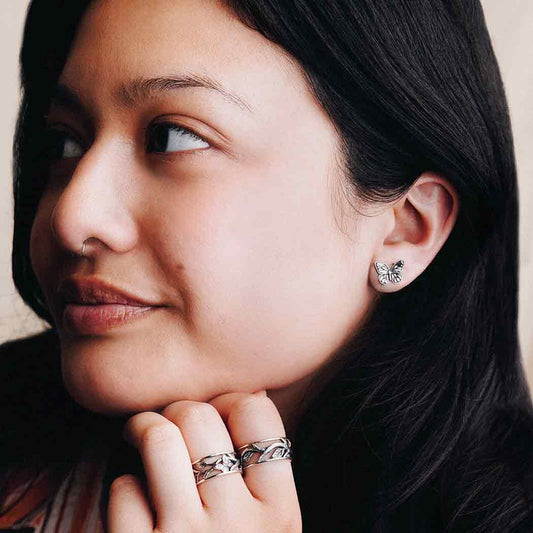Close-up of a woman wearing butterfly earrings and a ring, with a neutral background