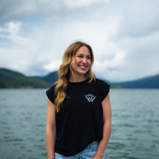 Woman wearing a black sleeveless shirt with a small logo that says "take me to the wildflowers"