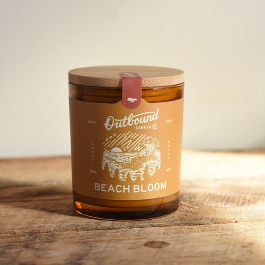 Candle labeled 'Beach Bloom' by 'Outbound Candle Co.' on a wooden surface.