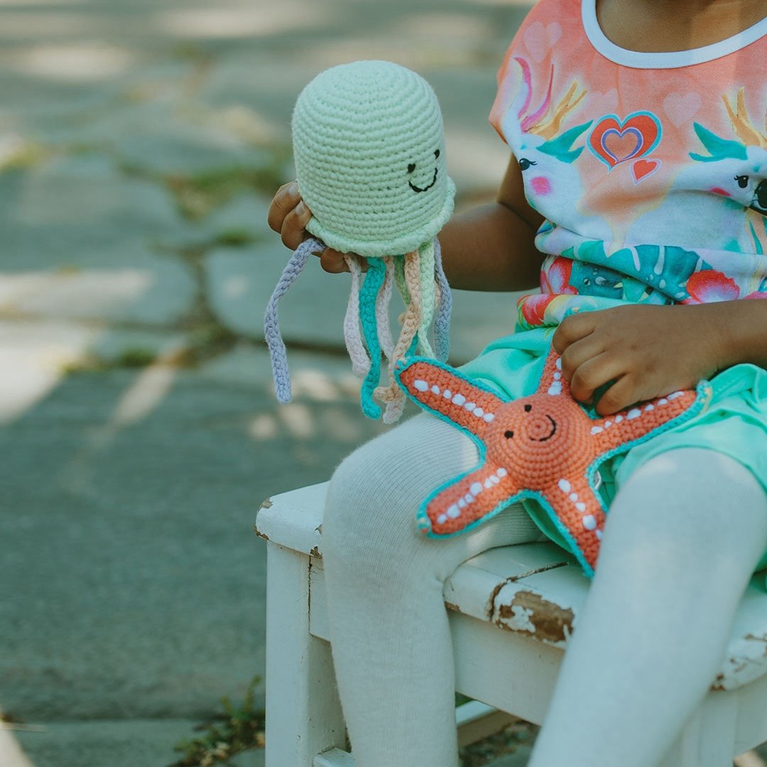 Child holding a green crochet octopus and orange starfish toy outdoors.