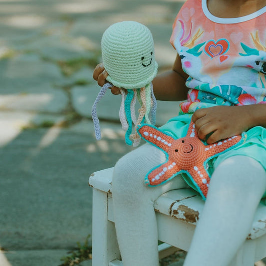 Child holding a green crochet octopus and orange starfish toy outdoors.