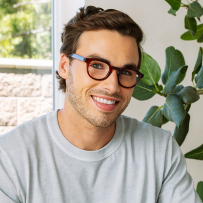 Man wearing glasses and a gray shirt with plants in the background
