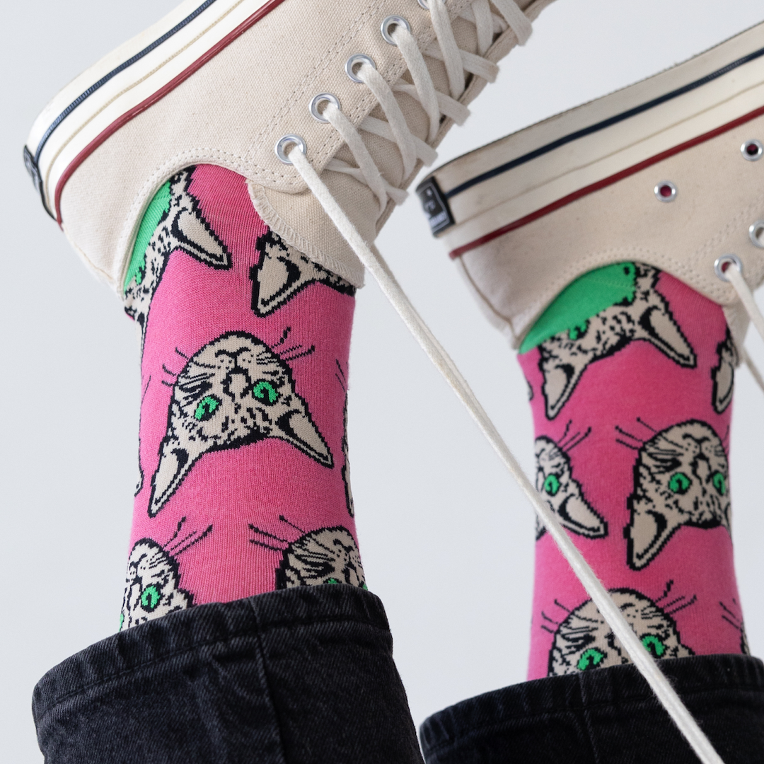 Pink socks with cat designs worn with white sneakers on a light gray background