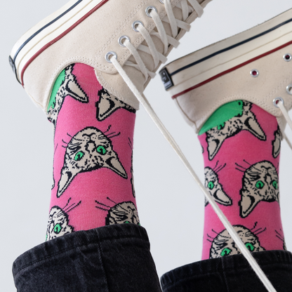 Pink socks with cat designs worn with white sneakers on a light gray background