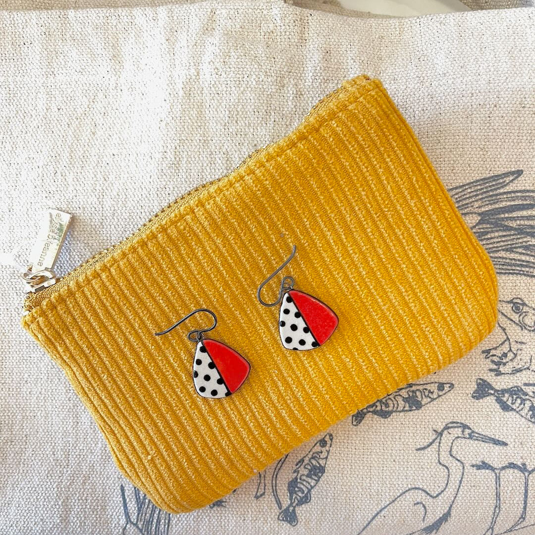 Mustard yellow textured pouch with red and black and white polka dot earrings on a patterned fabric background