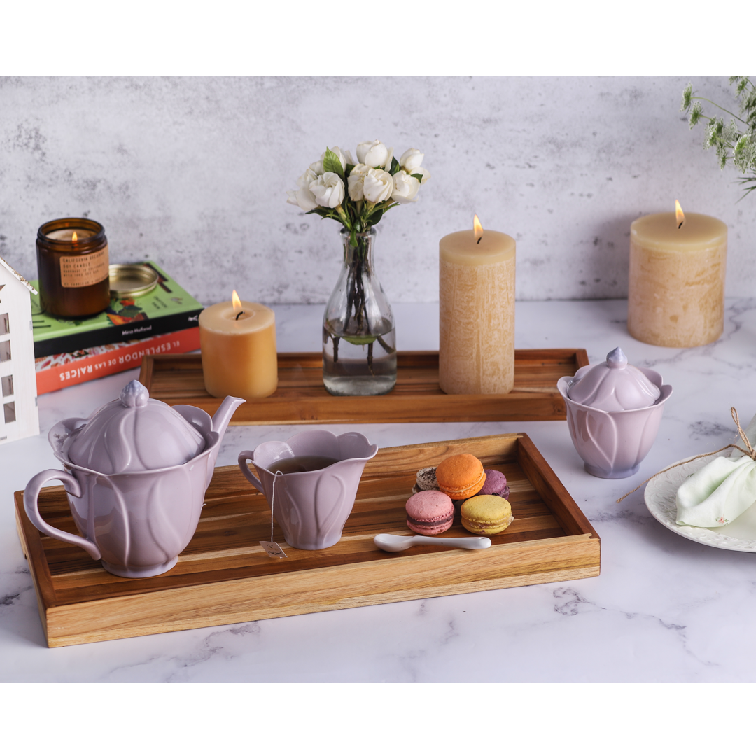 Wooden trays with tea set, candles, and macarons on a marble surface.