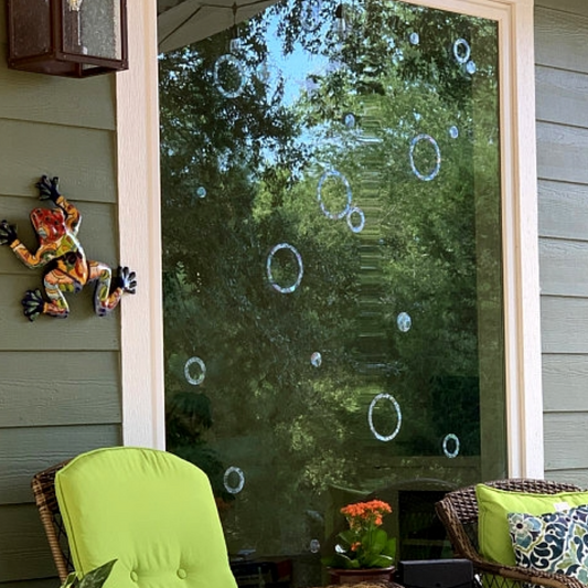 Outdoor setting with a window featuring iridescent rings and circles, chairs, and a decorative frog on a wall.