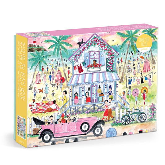 A jigsaw puzzle box featuring a colorful beach house illustration with people, palm trees, a pink convertible car, and a bicycle on a sandy beach. The box is shown at a three-quarter angle against a plain white background.