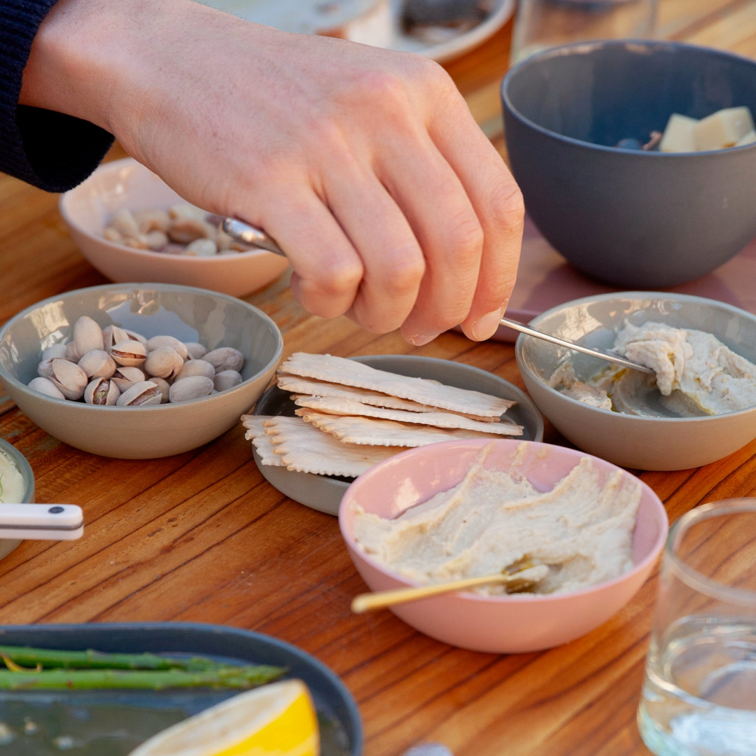 Person preparing a snack with crackers and spread on a wooden table.