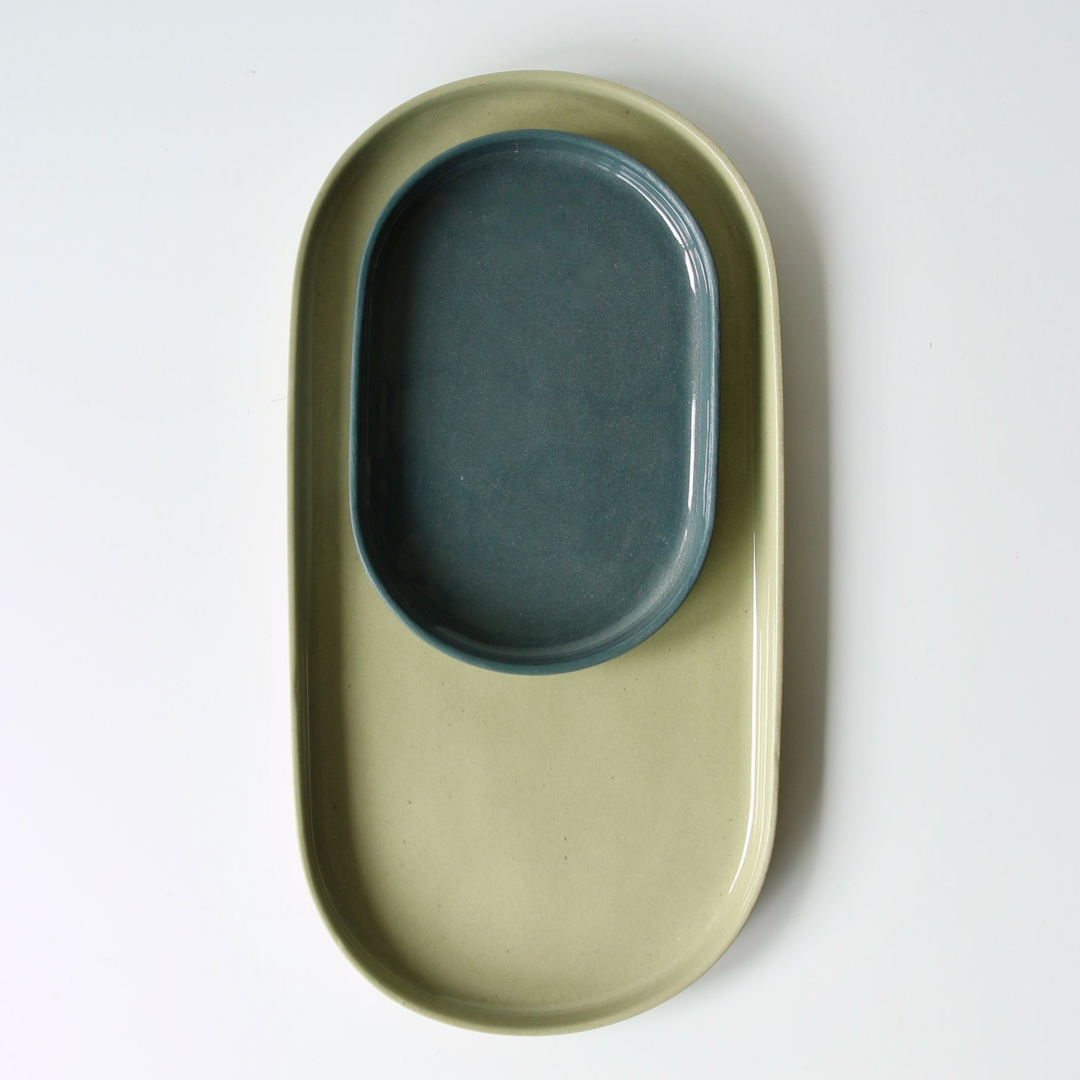 Green oval shaped ceramic dish with a smaller blue oval shaped dish nested inside on a white background