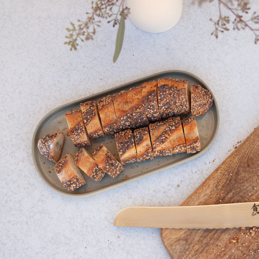 Sliced bread on a ceramic oval shaped dish with a knife on a light background