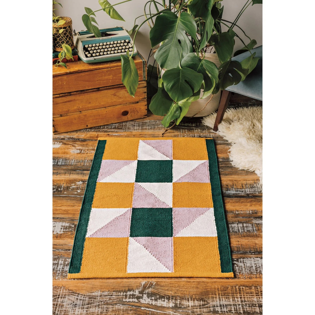 Multicolored geometric patterned rug on a wooden floor with plants and a vintage typewriter.