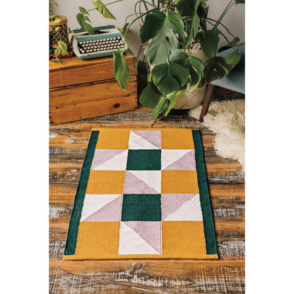 Multicolored geometric patterned rug on a wooden floor with plants and a vintage typewriter.