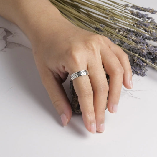 Hand wearing a silver ring with lavender flowers in the background