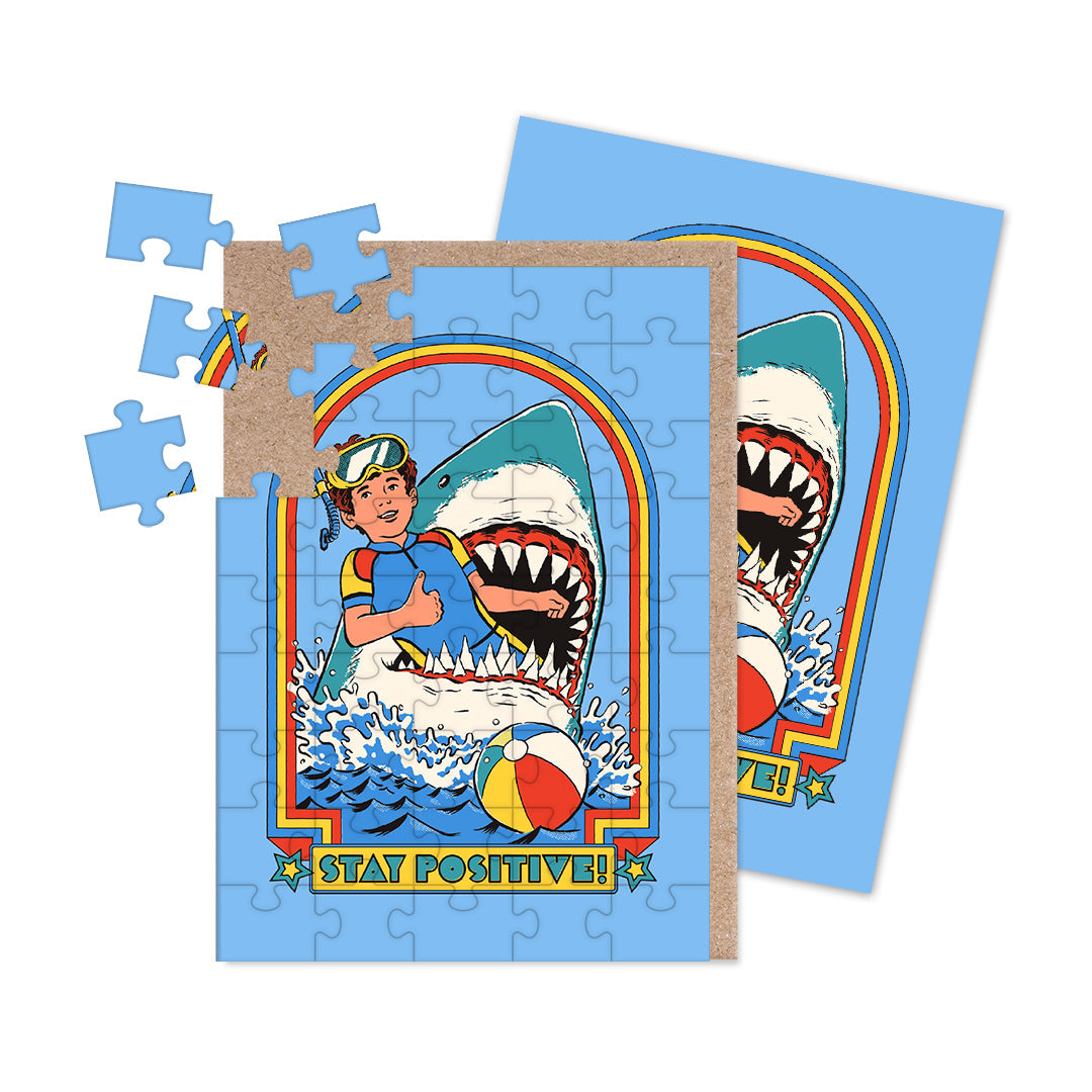 Jigsaw puzzle with a colorful design featuring a shark eating a person with text that reads "stay positive!," on a blue background.