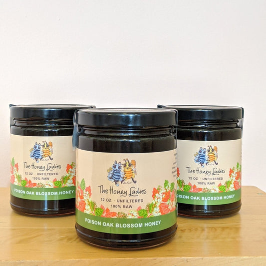 Three jars of 'The Honey Ladies' Poison Oak Blossom Honey on a wooden surface with a white background.