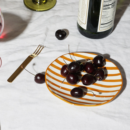 Striped plate with cherries on a white tablecloth with a bottle and glass in the background.