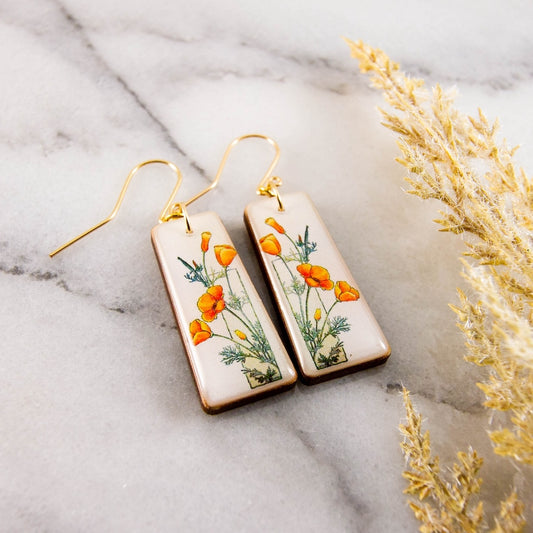 Pair of earrings with poppy design on a marble surface