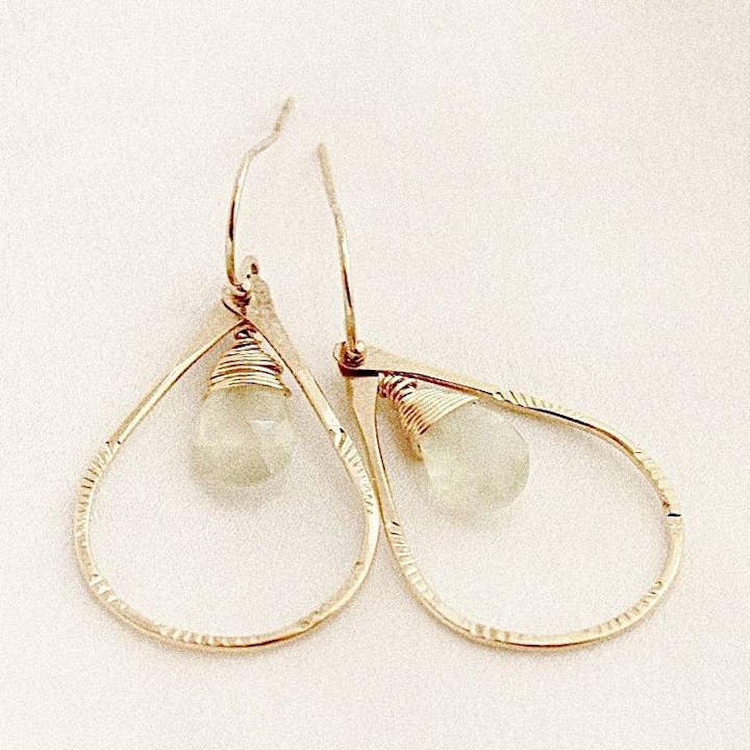 Gold hoop earrings with peridot gemstones on a light background