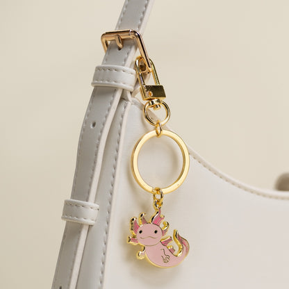 Pink axolotl keychain on a gold ring attached to a light gray strap.