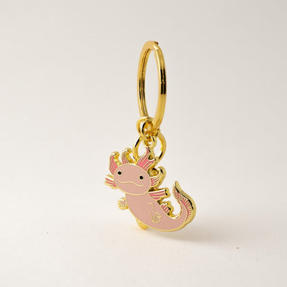 Pink axolotl charm with gold outline on a beige background