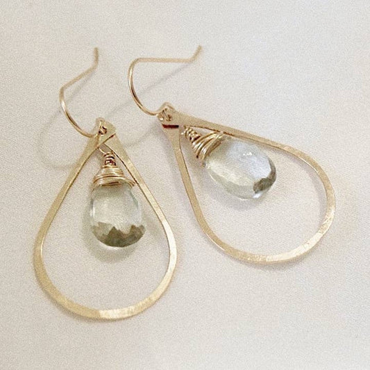 Gold hoop earrings with teardrop-shaped sage green gemstones on a light background