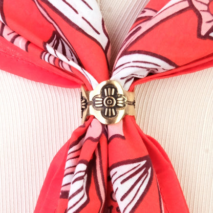 Red patterned bandana with a brass bandana ring on a textured beige background