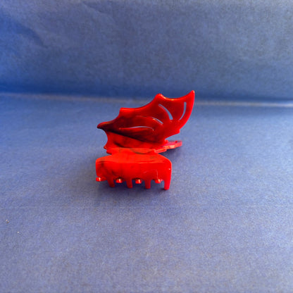 A red plastic bat shaped claw hair clip on a textured blue background.