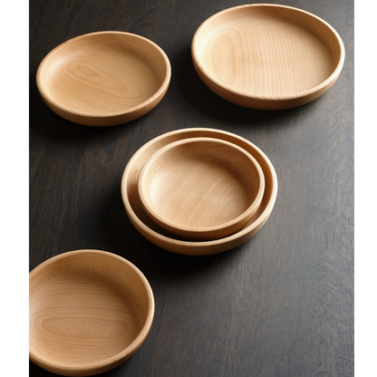 Four light natural wood bowls of varying sizes arranged on a dark wood surface, including one stack of nested bowls and three single bowls viewed from above.