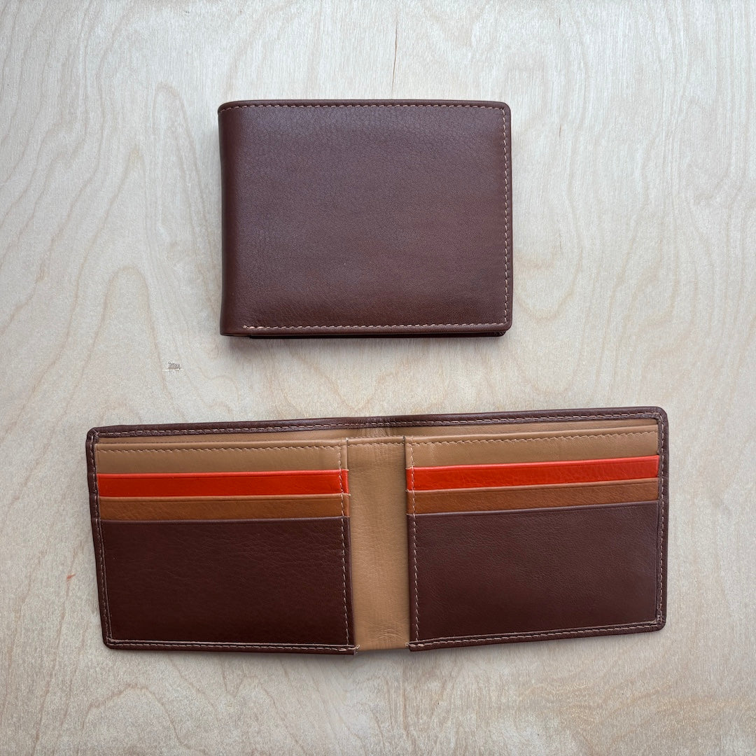 A dark brown leather bifold wallet shown closed at the top and open at the bottom on a light wood grain background. The open wallet features multiple card slots with accent stripes in tan, orange, and red.