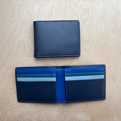 A dark navy blue leather bifold wallet shown closed and open on a light wood grain background. The open wallet reveals multiple card slots with blue, green, white, and light blue striped cards, and a bright blue center band.
