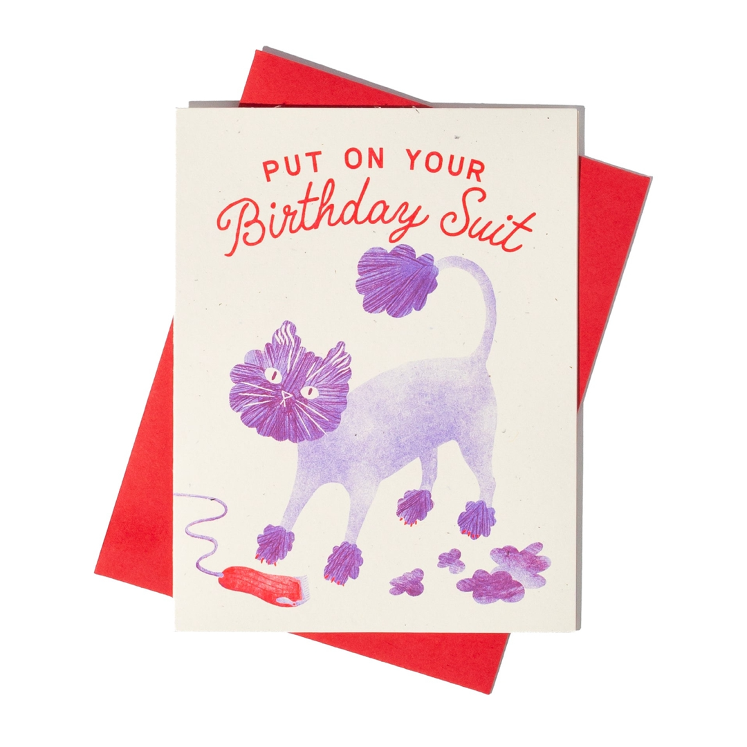 A novelty greeting card with a red envelope, featuring a cartoon cat that has been shaved to look like a lion with the text 'PUT ON YOUR Birthday Suit' in red script.