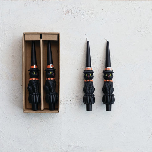 Black cat-shaped candles with witch hats on a white background