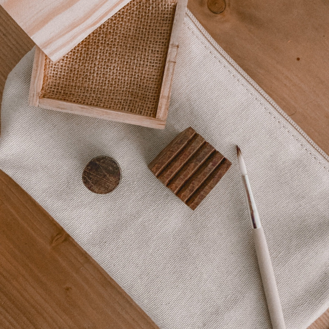 close up of a paintbrush, pine ink tray, a circle wooden block, and a square wooden block on a canvas pouch
