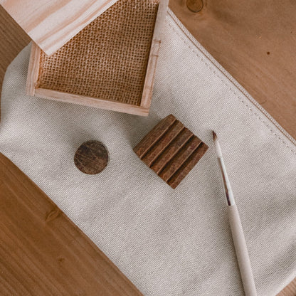 close up of a paintbrush, pine ink tray, a circle wooden block, and a square wooden block on a canvas pouch