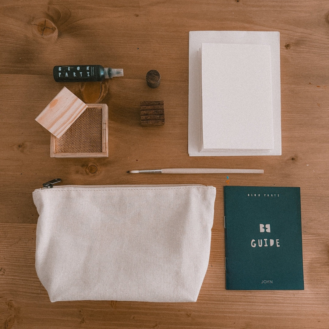 a bottle of ink, pine ink tray, 2 wooden blocks, cards, a paintbrush, canvas pouch, and block printing guide on a table 
