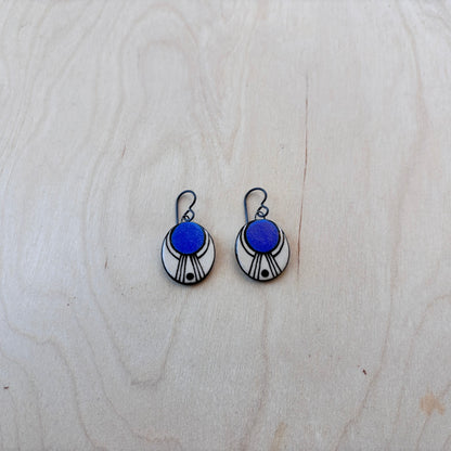 Pair of earrings with blue and white painted oval dangles on a light wooden surface