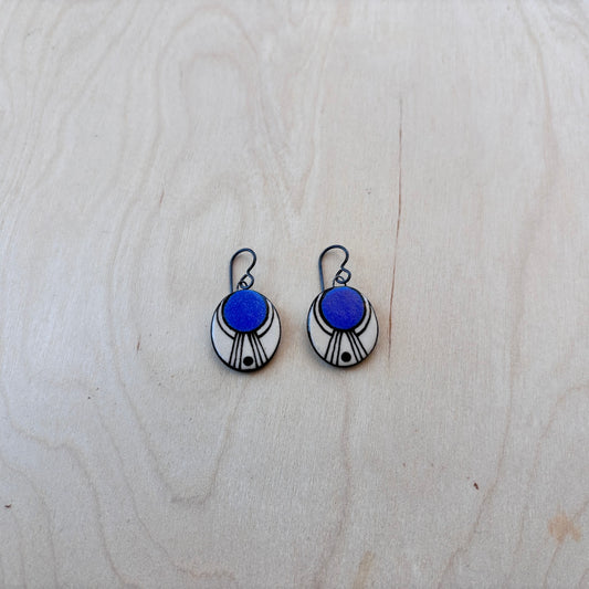 Pair of earrings with blue and white painted oval dangles on a light wooden surface