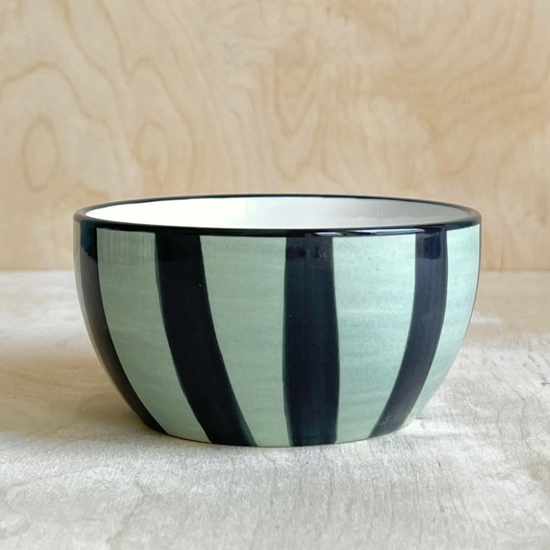 Ceramic bowl with dark blue and light green stripes on a light wooden background