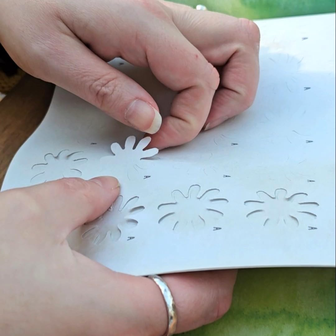 Close-up of hands holding a white sheet with floral-shaped cutouts over a green surface.