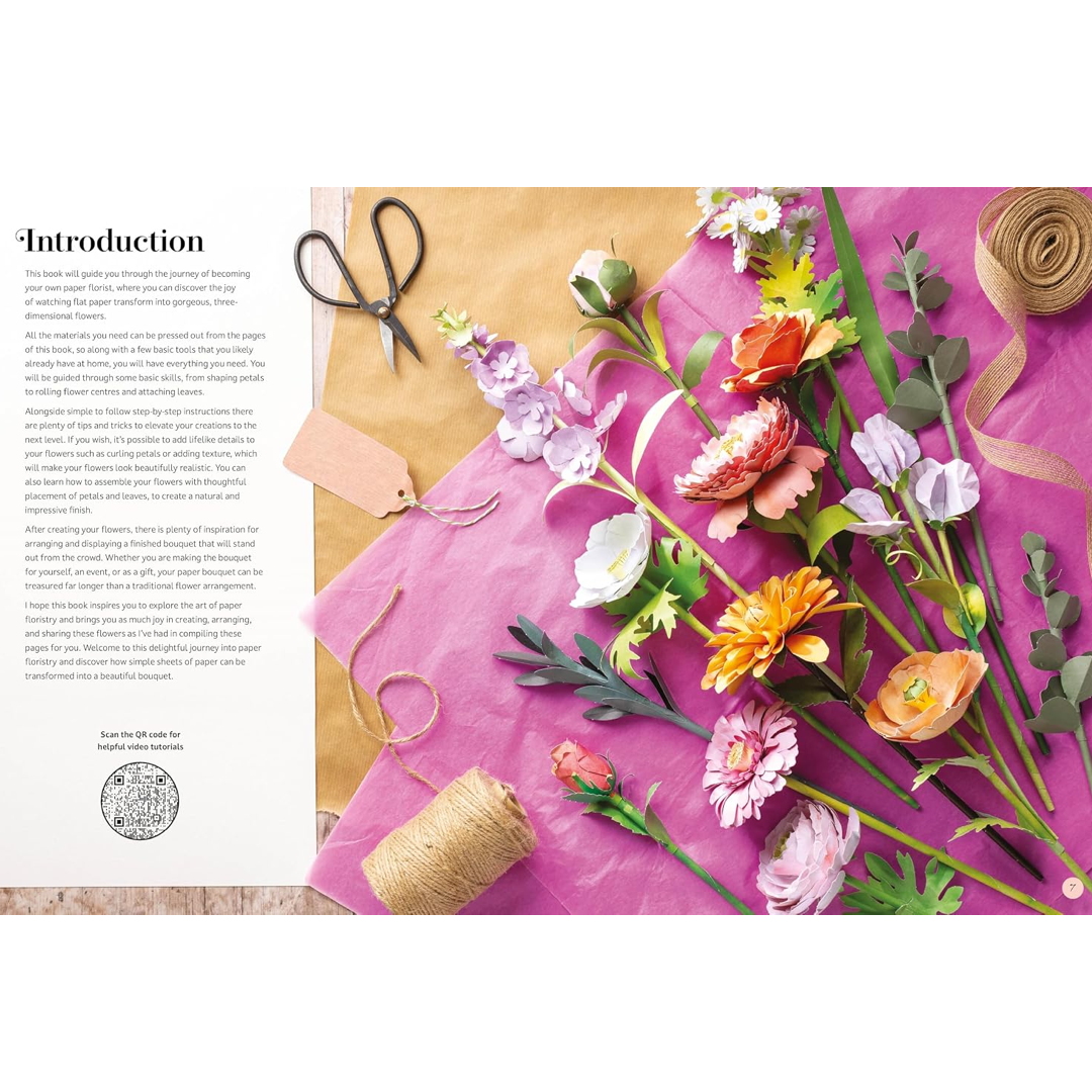 An open book spread showing a paper-flower making guide, with a bright pink sheet of paper, artificial flowers, twine, scissors, and a kraft paper background.