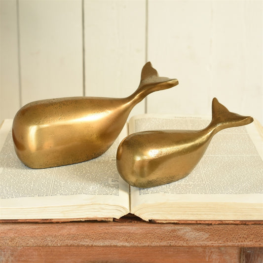 Two gold whale-shaped objects on an open book with a wooden surface and white paneled wall background.