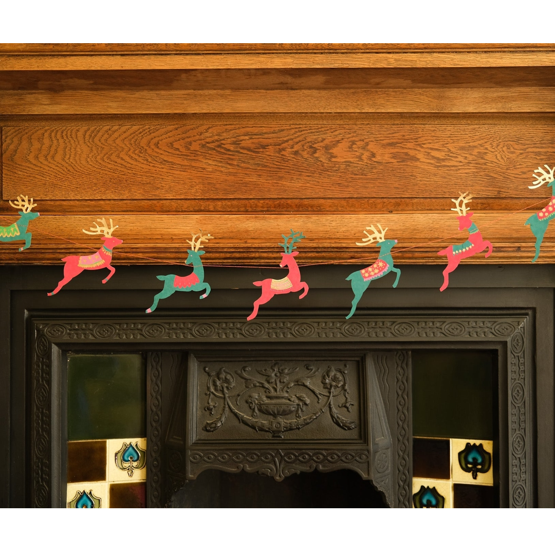 A festive Christmas garland featuring colorful paper reindeer cutouts in pink, teal, and green, hung across the mantel above a dark carved fireplace.