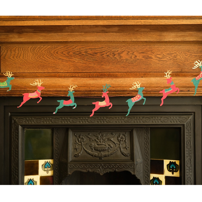A festive Christmas garland featuring colorful paper reindeer cutouts in pink, teal, and green, hung across the mantel above a dark carved fireplace.