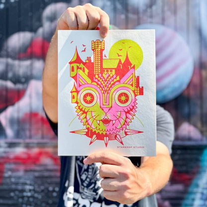 Person holding a colorful illustration of a creature with a castle on its head against a blurred background.