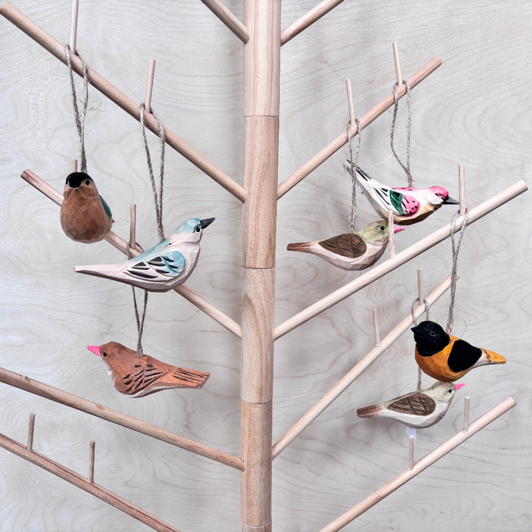 Decorative bird ornaments hanging on a wooden tree branch against a light gray background