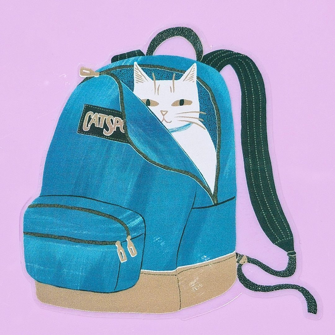 A blue backpack with a white cat peeking out from the top pocket, set against a solid light purple background. The backpack features a black patch with 'CATSPORT' written on it, a beige bottom base, and dark green straps.